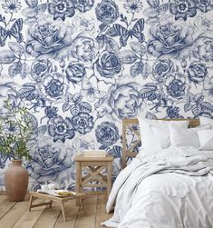 a bed sitting next to a wooden table on top of a hard wood floor under a blue and white floral wallpaper