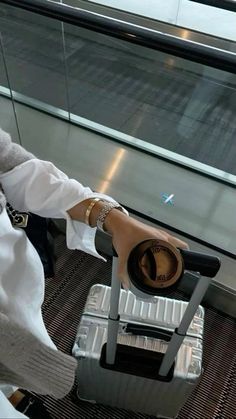 a woman sitting on top of a luggage bag next to an airport window with her hand on the handle