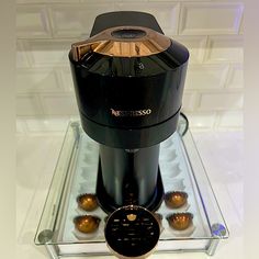 a black coffee maker sitting on top of a glass shelf next to some gold balls