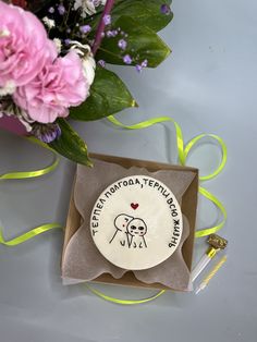 a white plate sitting in a box next to pink flowers and a green ribbon on a table