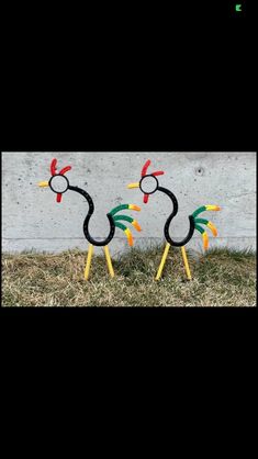 two birds made out of plastic sticks sitting on top of some grass next to a wall