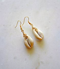 two seashells are hanging from gold earwires on a white surface,