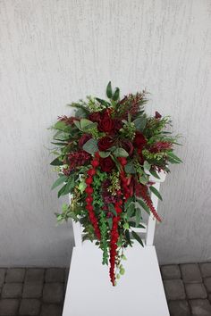 a bouquet of red flowers and greenery on a white pedestal in front of a wall