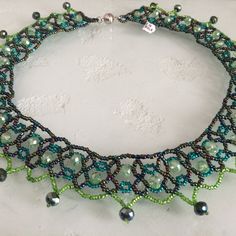 a green and black beaded necklace on a white surface