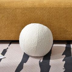 a large white ball sitting on top of a rug next to a yellow couch and book