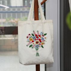 a white tote bag with flowers on it hanging from a wooden pole in front of a window