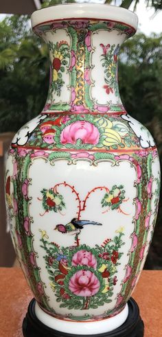 an ornate vase with flowers painted on it sitting on a table next to some trees