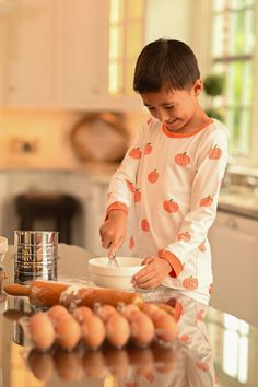 a young boy mixing something in a bowl on top of a kitchen counter next to eggs