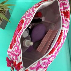 a pink and white bag with various items in it sitting on a blue table next to a potted plant