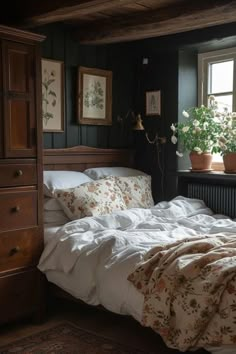 an unmade bed sitting next to a window with potted plants on the windowsill