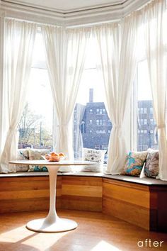 the sun shines through two windows in this room with wood floors and white drapes