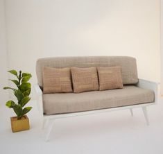 a couch with four pillows on it next to a potted plant