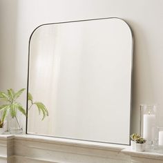 a mirror sitting on top of a mantle next to a potted plant and candles