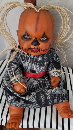 a creepy looking doll sitting on top of a striped pillow in front of a wall