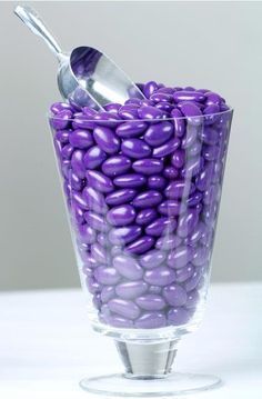 a glass filled with purple candy beans and a silver spoon in it's holder