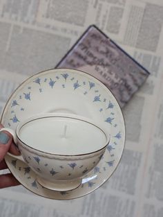 a person holding a teacup and saucer with a book on the table in the background