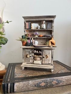 an old fashioned wooden cabinet on top of a book shelf with pots and plants in it