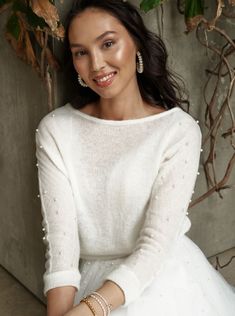 a woman in a white dress sitting on the ground with her arms crossed and smiling