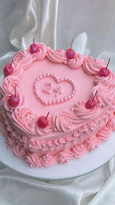 a heart shaped cake with pink frosting and cherries on top, sitting on a white table cloth