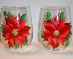 two wine glasses decorated with red flowers and green leaves are sitting on a white surface