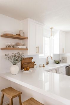 a white kitchen with marble counter tops and open shelving above the sink, along with wooden stools