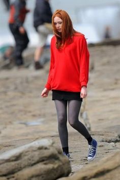 a woman with red hair is walking on the beach wearing black and grey tights