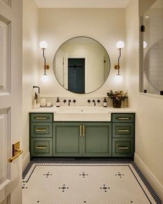 a bathroom with green cabinets and a round mirror above the sink, along with black and white tile flooring