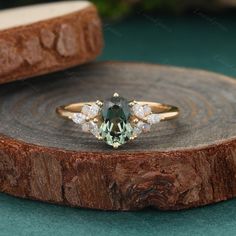 a green and white diamond ring sitting on top of a wooden slice