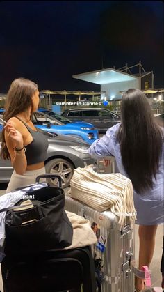 two women standing next to each other with luggage in front of them at an airport