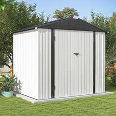 a white and black shed sitting on top of a lush green field next to a wooden fence