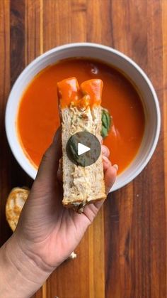 a person holding a piece of bread in front of a bowl of soup