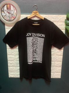 a black t - shirt with the words joy division on it hanging next to a clock