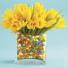 a vase filled with lots of yellow flowers on top of a blue table next to candy