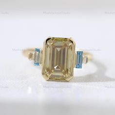 an emerald and blue diamond ring on a white surface with the center stone in yellow gold