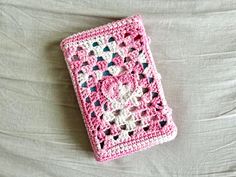 a pink crocheted book laying on top of a white bed sheet with black dots