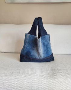 a denim bag sitting on top of a white bed next to a painting hanging above it