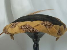 Simply a delightful and rare hat.  This Tilt hat is meant to wear, well tilted - to the side or front.   The crown is black and the exterior band is a beautiful weave of fancy brocade and flat marigold felt. It has two wire clips covered in the same material marigold interior band.  The graceful slim feather is 12.5 inches and starts at the broach and curves across the font. The broach crystals have been completely replaced because  the original was missing a few pieces. Please look closely at the last picture. The interior appears to have a large water mark that does not show through to the exterior. Pre-owned: no tears, stains or holes (see last photo) Crown Circumference 22.5 inches Crown depth 4.5 inches Brim depth 1.75 inches  All my items come from my clean smoke free home. Thank you Gold Leaf Bill Hat, Vintage Adjustable Fascinator With Structured Crown, Vintage Costume Hats With Structured Crown, Victorian Brimmed Costume Hats And Headpieces, Victorian Brimmed Costume Hat, Vintage Black Ceremonial Hat, Victorian Curved Brim Costume Hat, Black Vintage Ceremonial Hat, Victorian Cloche Hat For Vintage Events