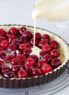 a cherry pie with cream being poured on top and cherries in the bottom crust