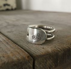 two silver rings sitting on top of a wooden table next to a flower design ring