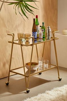 a bar cart with drinks and glasses on it in front of a potted plant