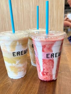 three drinks sitting on top of a wooden table with blue straws in each cup