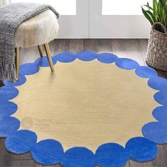 a round rug with blue scalloped edges on a wooden floor next to a chair and potted plant