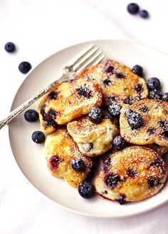 blueberry pancakes with powdered sugar on a plate next to a fork and spoon