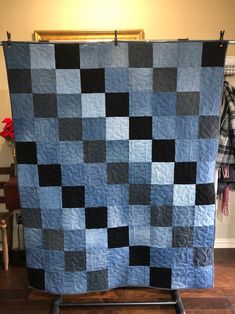 a blue and black quilt is hanging on a rack in front of a chair with a plaid blanket