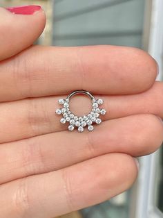 a woman's hand holding an open nose ring with small white stones on it