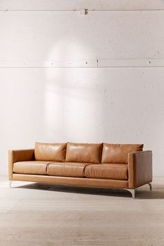 a tan leather couch sitting on top of a wooden floor next to a white wall