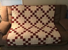 a red and white quilt sitting on top of a couch next to a brown chair