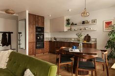 a living room and kitchen area with green couches, table and shelves on the wall