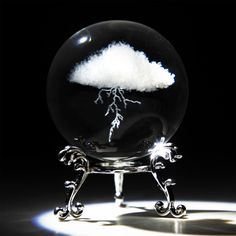 a glass ball with a cloud and lightning in it on a black background, surrounded by silver ornaments