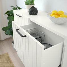 a white cabinet with two baskets on top and some lemons in the bottom drawer